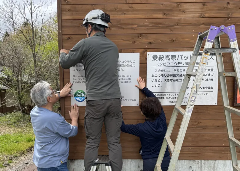 乗鞍高原のバットハウスで、クビワコウモリの保護活動の一環として案内看板を設置している3人の様子